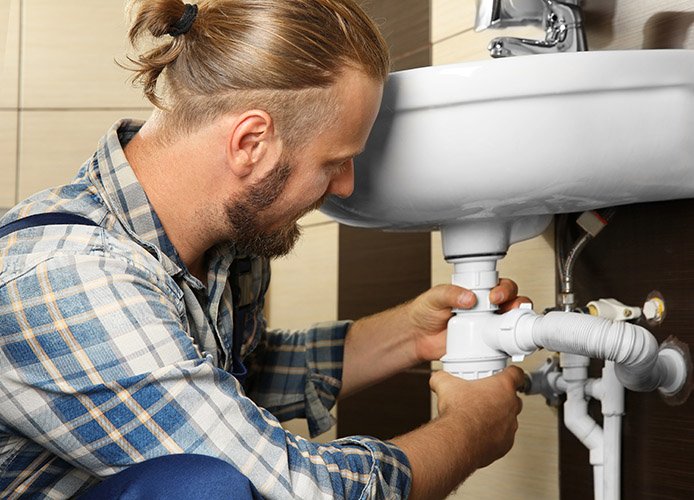 Handsome plumber assembling sink pipes in bathroom, close up vie
